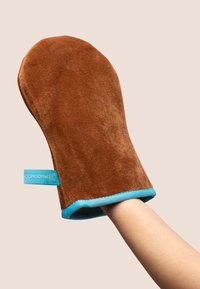 Mitten de bronzage en peluche beige avec une texture douce et un contour bleu, comportant une étiquette. Conçu pour s'adapter à la main pour une application facile.