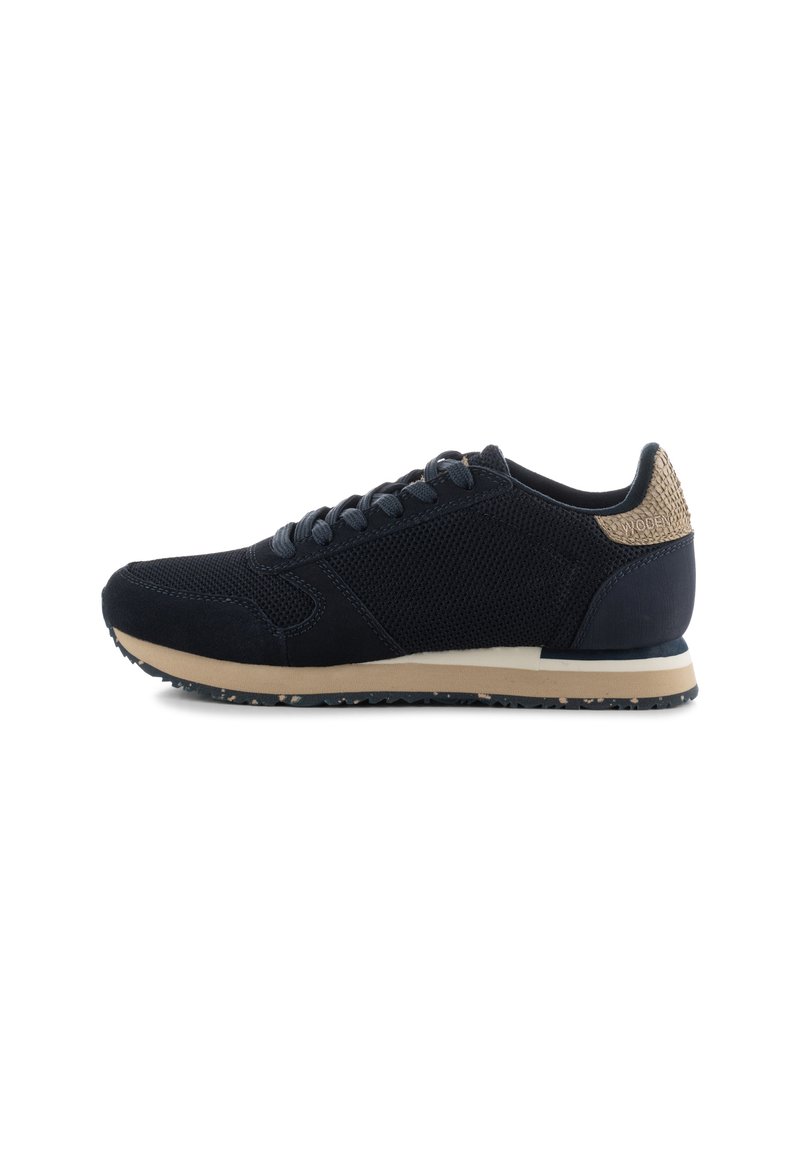 Black athletic shoe with mesh and suede upper, dark laces, contrasting beige sole, and textured heel accent.