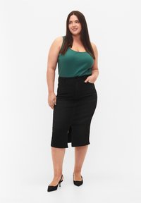 Falda lápiz de mezclilla negra con una abertura frontal, combinada con una camiseta sin mangas verde. La modelo lleva zapatos de tacón alto negros. Fondo limpio.