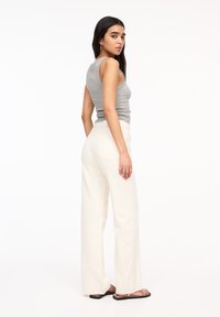 Svetlo sivi top brez rokavov v kombinaciji z belimi jeans hlačami širokega kroja z visokim pasom. Model ima dolge temne lase in stoji na enobarvni beli podlagi.