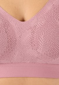 Bralette en dentelle rose avec un décolleté en V, des motifs de feuilles élaborés et une large bande élastique texturée au bas.