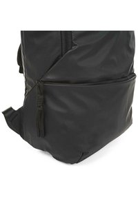 Mochila negra con textura suave y brillante. Cuenta con un bolsillo lateral con cierre, correas ajustables y un diseño angulado único.