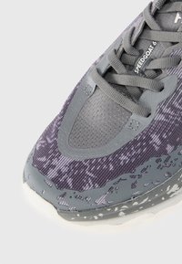 Lila und grauer Sportschuh mit strukturiertem Mesh-Obermaterial, verstärkter Zehenkappe und gesprenkelter Sohle. Verfügt über eine gepolsterte Zunge und Schnürsenkel.