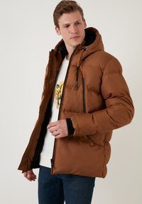 Brun pufferjakke med hætte, der har en lynlåslukning foran, elastiske håndled, og sidelommer; glat tekstur med kviltet design.