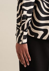 Camicia a righe zebrate in bianco e nero, con design colletto, maniche con bottoni e una texture di tessuto liscia.