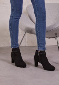 Mustat mokkanahkasaappaat, joissa on pyöreä kärki ja tukevat korot. Varustettu vetoketjulla ja nahkavyön yksityiskohdalla nilkassa.