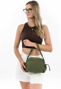 Borsa a spalla verde oliva con manico intrecciato, scomparti con zip e una texture di tessuto morbido. Presenta un logo impresso sulla parte anteriore.