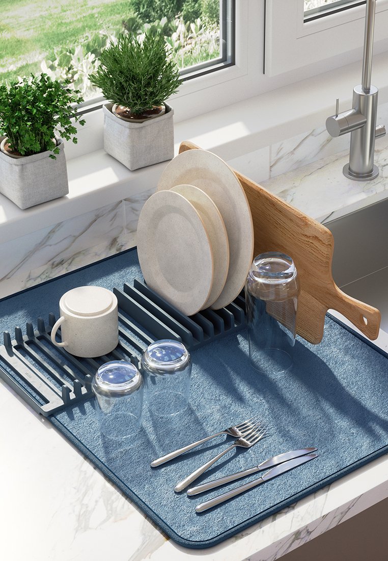 Eine blaue Abtropfmatte hält sauberes Geschirr, darunter drei runde Teller, eine Tasse, zwei Glasschraubgläser, ein Holzschneidebrett und Edelstahlbesteck.