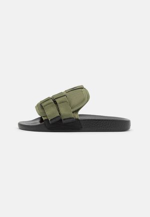 Sandalo con cinturino in velcro in tessuto verde e suola nera texturizzata. Presenta due cinturini regolabili e design con punta aperta. Leggero e casual.