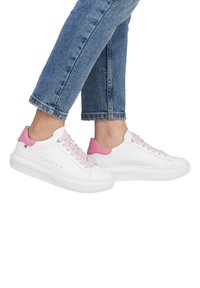 Baskets blanches avec des accents roses et des lacets tressés. Caractérisées par une semelle épaisse et de subtiles perforations sur les côtés. Portées avec un jean bleu retroussé.