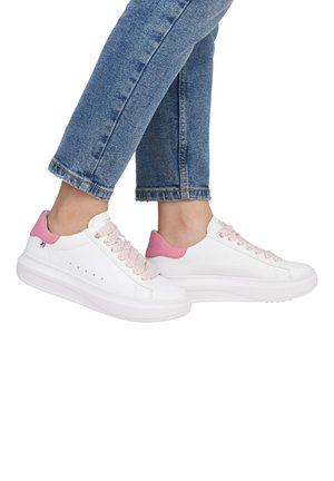 Sneakers bianchi con accenti rosa e lacci intrecciati. Presentano una suola spessa e piccole perforazioni sui lati. Indossati con jeans blu risvoltati.