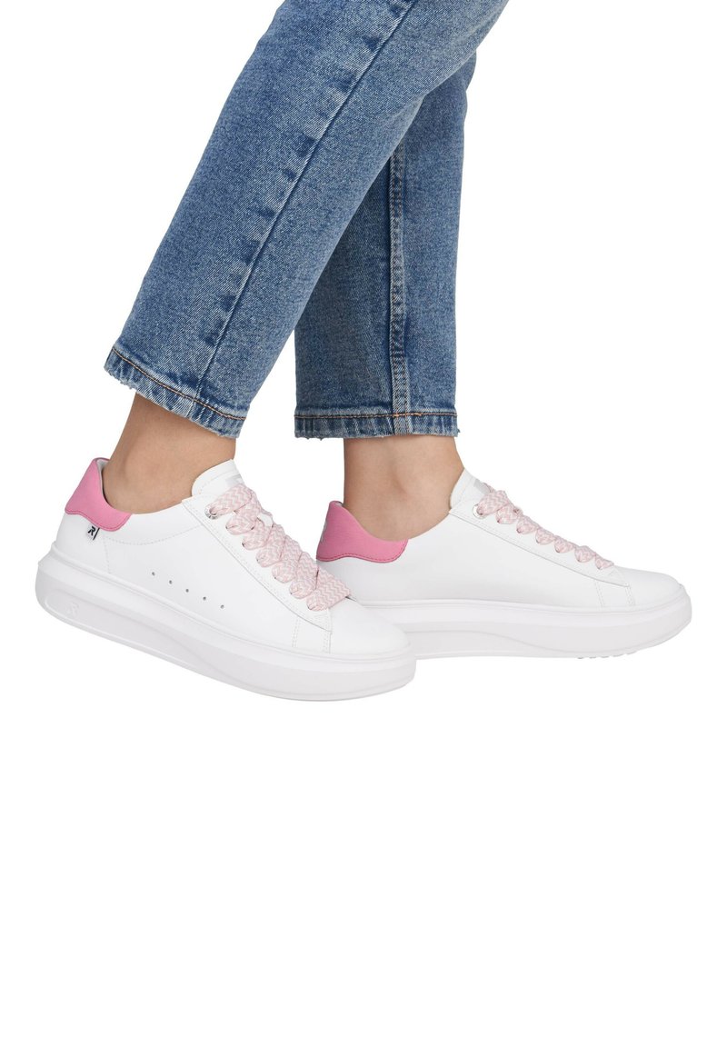 Baskets blanches avec des accents roses et des lacets tressés. Caractérisées par une semelle épaisse et de subtiles perforations sur les côtés. Portées avec un jean bleu retroussé.