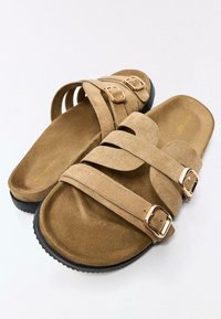 Sandales en daim marron avec deux brides réglables et boucles dorées. Texture douce, semelle plate avec une semelle extérieure noire texturée.