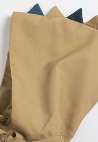 Tissu beige avec trois accents triangulaires bleus et verts en haut, présentant une texture lisse et un design plié.