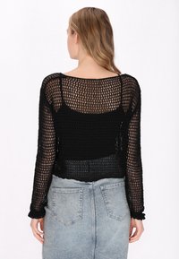 Čierny pletený crop top s dlhými priesvitnými rukávmi a voľným strihom. Má široký výstrih a textúrovaný otvorený vzor.