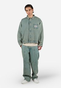 Chaqueta de denim azul claro con un bolsillo en la parte frontal, combinada con pantalones de pierna ancha a juego. Zapatillas blancas completan el atuendo.