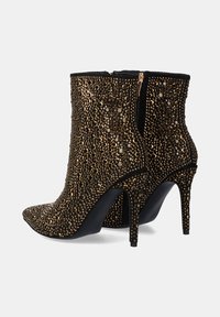 Botas negras hasta el tobillo con punta afilada, cubiertas de tachuelas doradas y plateadas, con un tacón alto y cierre con cremallera en la parte posterior.