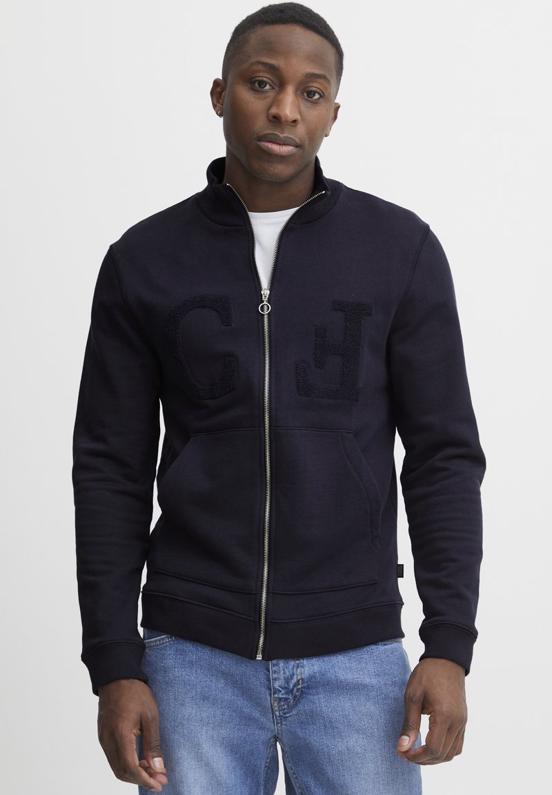 Marineblauer Zip-Hoodie mit hohem Kragen, zwei Fronttaschen und strukturierten "C"- und "H"-Buchstaben. Hergestellt aus weichem Material mit taillierter Passform.