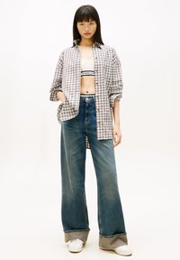 Camisa de botones de gran tamaño con estampado de cuadros en tonos claros, vaqueros de talle alto y pierna ancha, y zapatillas blancas con detalle de puño en capas.