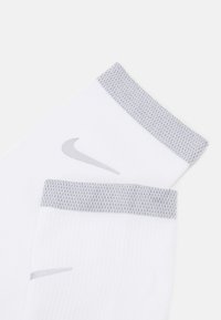 Baltos sportinės kojinės su šviesiai pilkais įlinkimais, ant šono matomas mažas pilkas Nike swoosh logotipas. Minkšta, tekstūruota medžiaga.