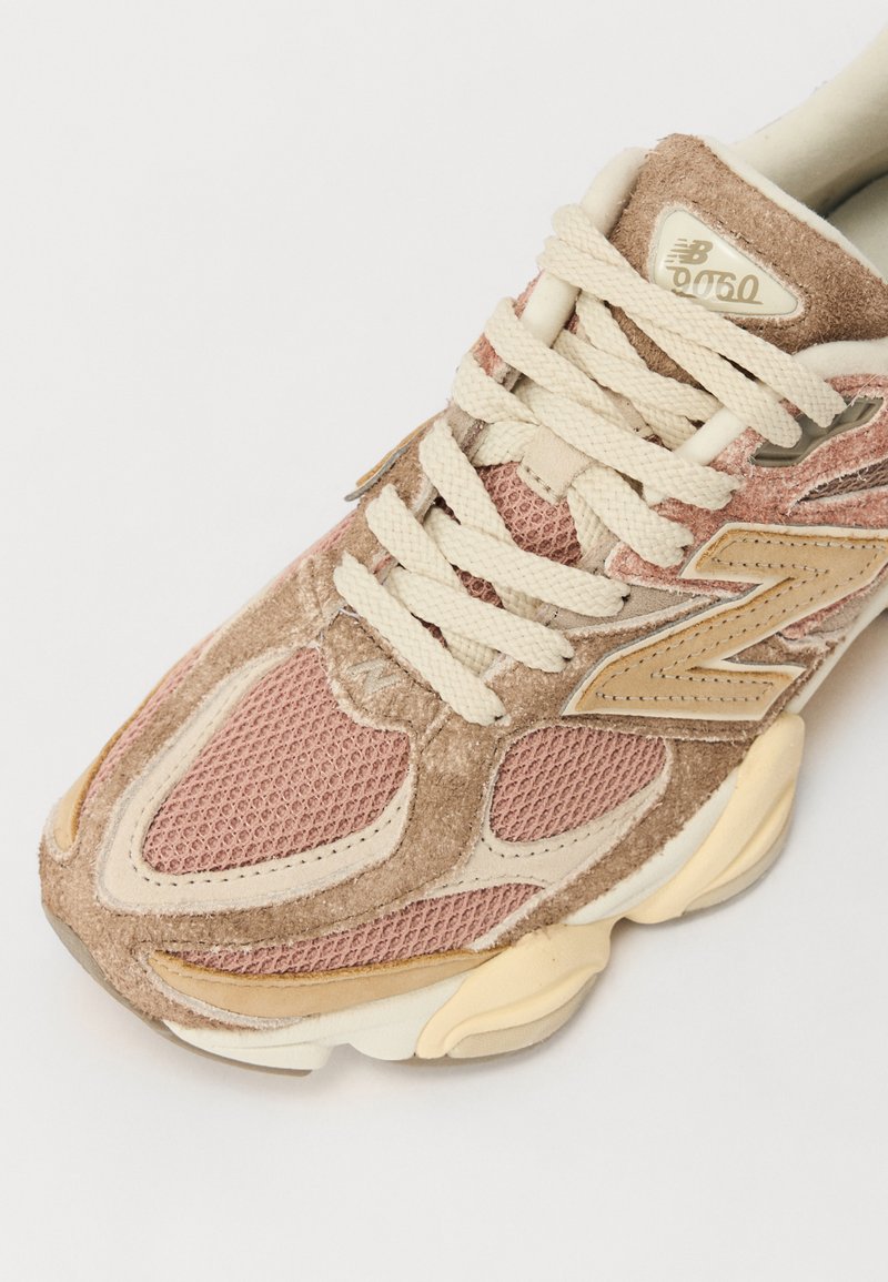 Sneaker aus einer Kombination von pinkem Mesh und braunem Wildleder, mit cremefarbenen Schnürsenkeln und Akzenten. Auffälliges New Balance-Logo in Gold an der Seite.