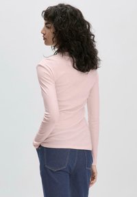 Langärmliges, figurbetontes Hemd aus weichem pinkem Material mit glatter Textur und rundem Ausschnitt. Kombiniert mit dunkelblauen Jeans.