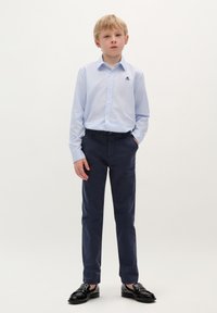 Camicia azzurra chiara con un piccolo logo, pantaloni blu scuro e scarpe nere lucide, creando un outfit formale per bambini.