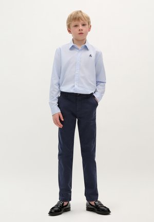 Camicia azzurra chiara con un piccolo logo, pantaloni blu scuro e scarpe nere lucide, creando un outfit formale per bambini.