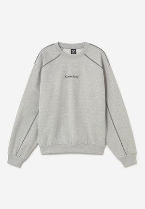 Gaiši pelēks apaļš kakls džemperis ar redzamu melnu šuvumu un "Kaotiko Society" tekstu izšūtu krūšu centrā.