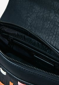 Schwarze strukturiert Lederhandtasche mit Reißverschluss. Das Innenfutter hat eine glatte Beschichtung, eine kleine Reißverschlusstasche und farbige Akzente auf der Außenseite.