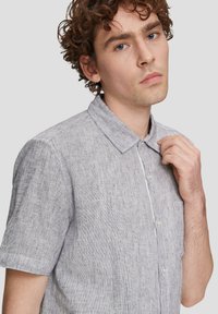 Kortarmig shirt van lichtgrijze stof met een gestructureerd patroon, knoopsluiting aan de voorkant en een klassieke kraag. Beschikt over één borstzak.