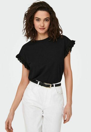 Top negro de manga corta con un borde de encaje con forma de concha, combinado con pantalones blancos de talle alto y un cinturón negro con hebilla dorada.