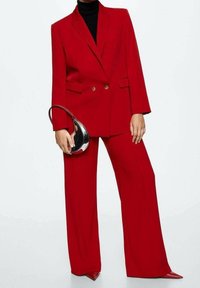 Rød dobbeltbrystet blazer med guldknapper og vide bukser, parret med en elegant sort turtleneck og en rund sort og sølv taske.
