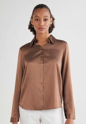 Blusa de satén marrón con un cierre frontal de botones, cuello, mangas largas y un dobladillo ligeramente curvado. Textura suave con botones a juego.