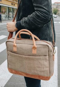 Canvas messenger bag in khaki with leather accents; features two top handles, a shoulder strap, and a zippered main compartment.