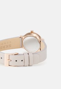 Round watch with a rose gold metal case and a light grey leather strap. Features a minimalist design with smooth textures and a secure buckle.