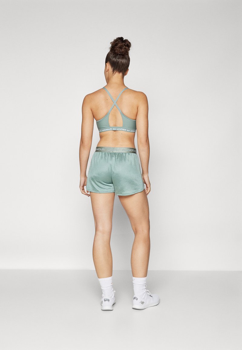 Conjunto atlético verde claro que incluye un sujetador deportivo de espalda cruzada con recorte y pantalones cortos a juego. Textura suave y detalles de cinturilla elástica.