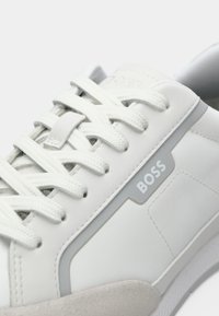 White leather sneaker with textured white laces, gray trim, and "BOSS" logo on the side near the sole.
