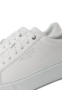 Adidași din piele albă cu vârf rotund, șireturi plate, cusături tonale și logo embossat pe lateral. Textură netedă cu un design elegant.