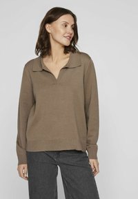 Suéter de punto marrón con cuello en V y solapas, puños y dobladillo acanalados, corte casual, combinado con pantalones de mezclilla de pierna ancha en gris oscuro, frente a un fondo neutro.