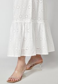 Vit bomullsklänning med blommig hålmönster och volangfåll, tillsammans med klara klacksandaler med transparent rem och blockklack.