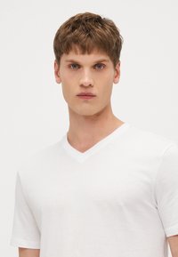Weißes V-Ausschnitt-T-Shirt aus Baumwollmischung mit kurzen Ärmeln und glatter Textur in einem schlichten Design.