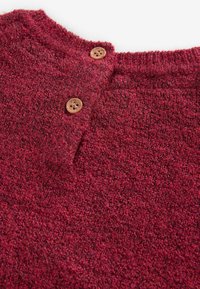 Bordeauxfarbener Strickpullover mit einem strukturierten, gefleckten Muster. Mit einem runden Ausschnitt und zwei braunen Knöpfen am Halsöffnungsbereich.