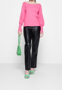 Rosa schulterfreier Pullover, schwarze Kunstlederhose, grüne Handtasche und grüne offene Schuhe mit Absatz. Weicher Stoff und figurbetontes Design.