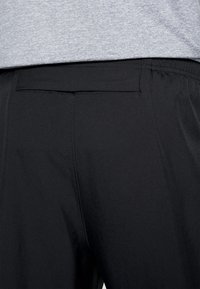 Achteraanzicht van een persoon die zwarte broek met elastische tailleband en achterzak draagt, in combinatie met een lichtgrijze heathered shirt.