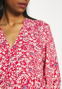 Abito floreale in rosa con motivi bianchi e blu. Presenta un collo a V, maniche corte e un tessuto textured con una vestibilità ampia.