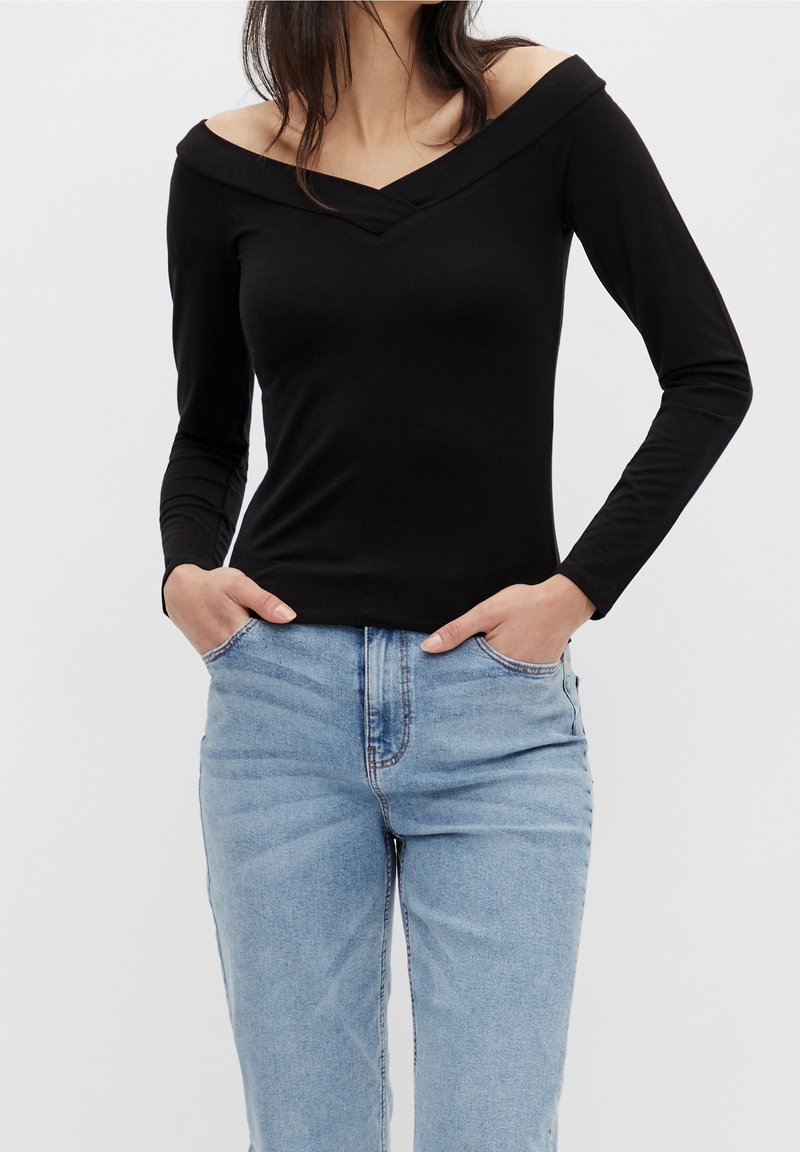 Svart, off-the-shoulder långärmad topp med djup V-ringning. Slät tyg, åtsittande design. Matchas med ljusblå, högmidjade jeans.