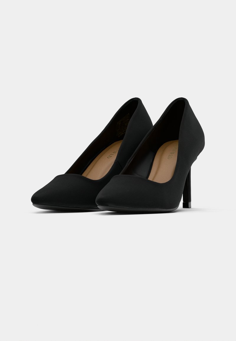 Une paire de pompes noires à talons hauts et à bout pointu avec une finition mate lisse, présentée sur un fond gris clair uni.