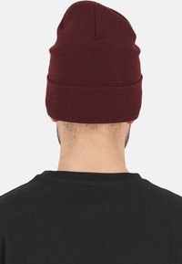 Burgundy knit beanie with a soft texture, featuring a fitted design that tapers at the top and a folded cuff at the base.