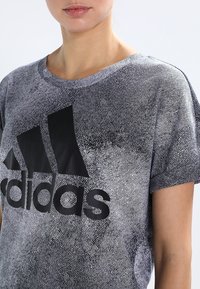 Black and white short-sleeve t-shirt with a textured pattern and a large black Adidas logo on the front. Crew neck design.